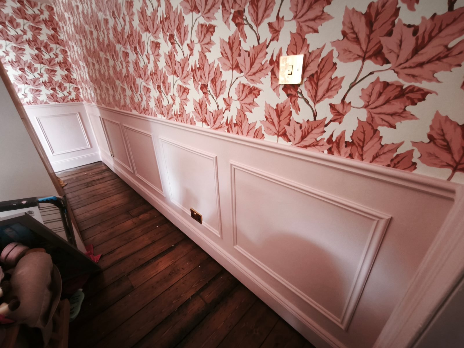 Pink wainscoting beneath leaf wallpaper